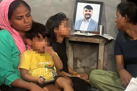 A woman, a child with a blurred face and a man seated near a framed portrait.