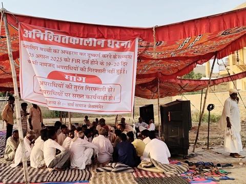 People seated beneath a canopy at a gathering with a Hindi banner.