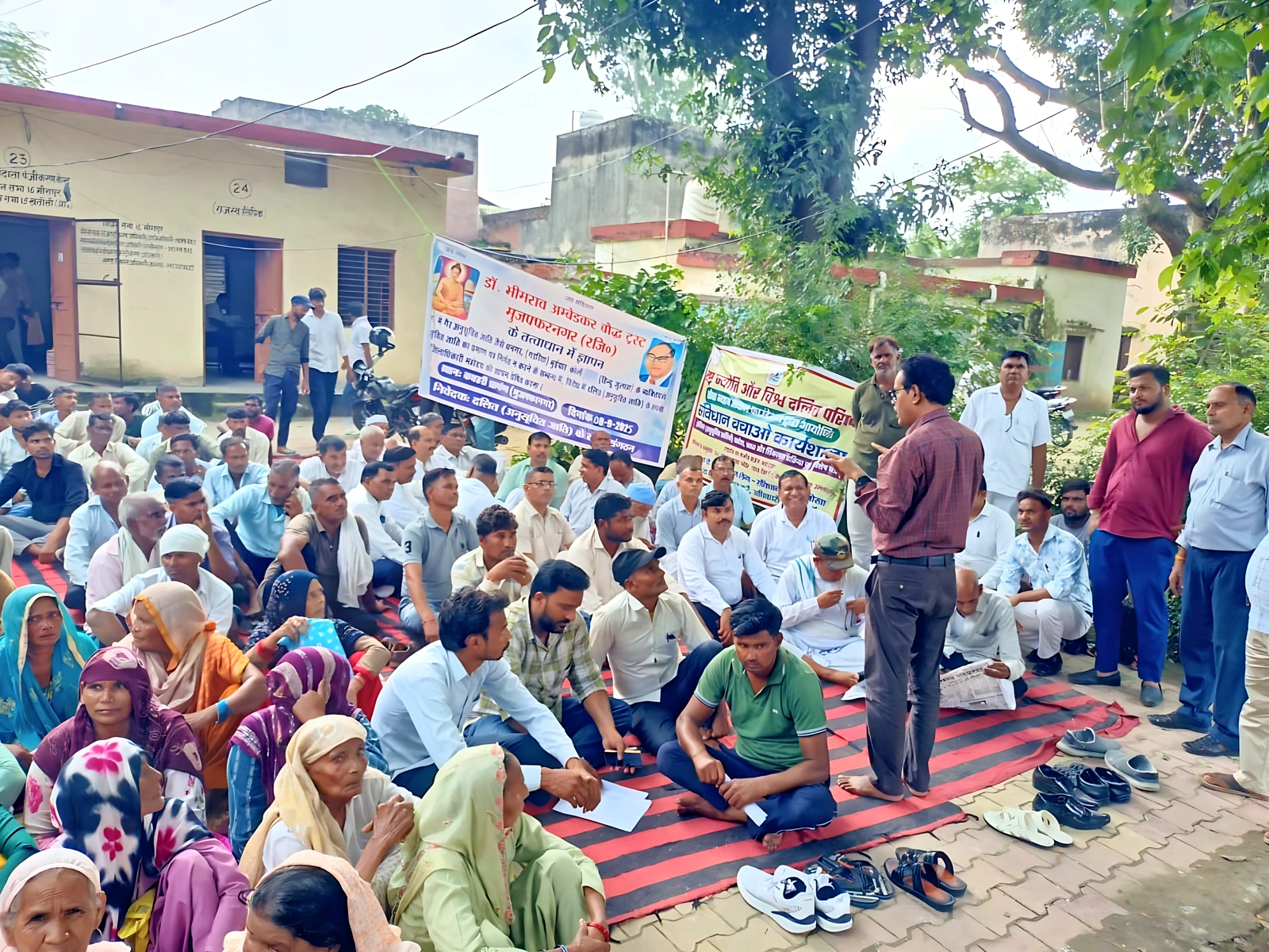 A group seated outdoors while a man speaks into a microphone.